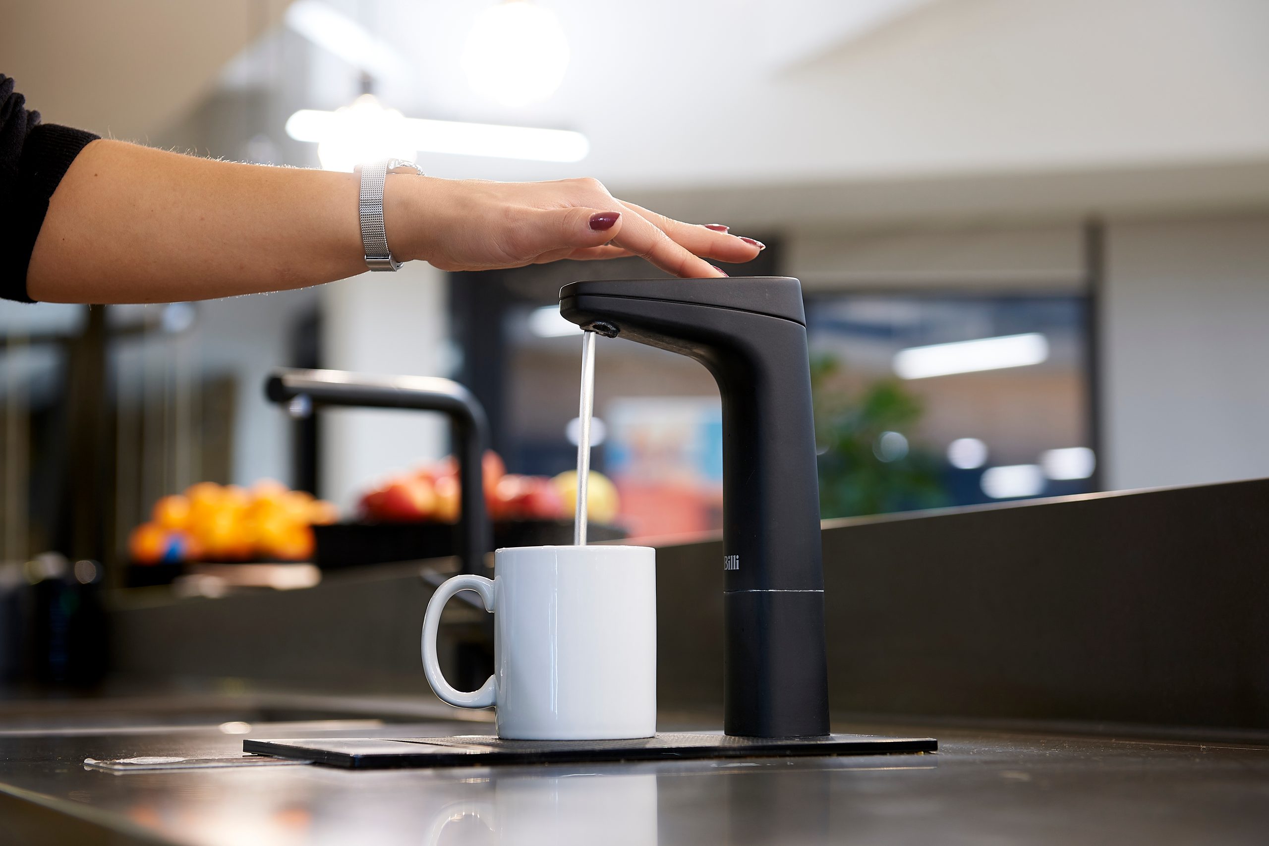 Hand pressing a matte black Billi XT dispenser to fill a mug in an office kitchen