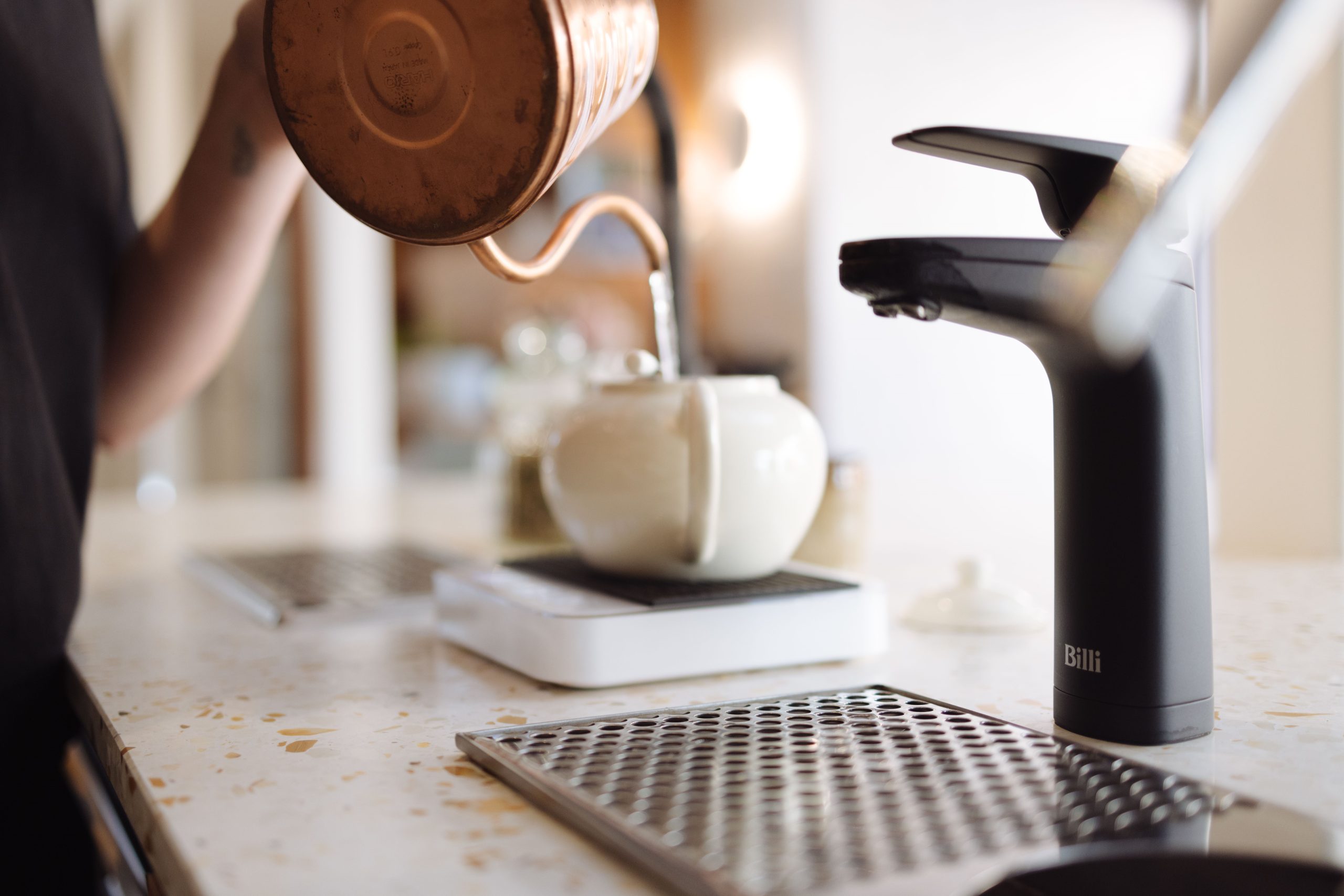 Barista pouring tea beside a matte black Billi XL dispenser at a restaurant counter