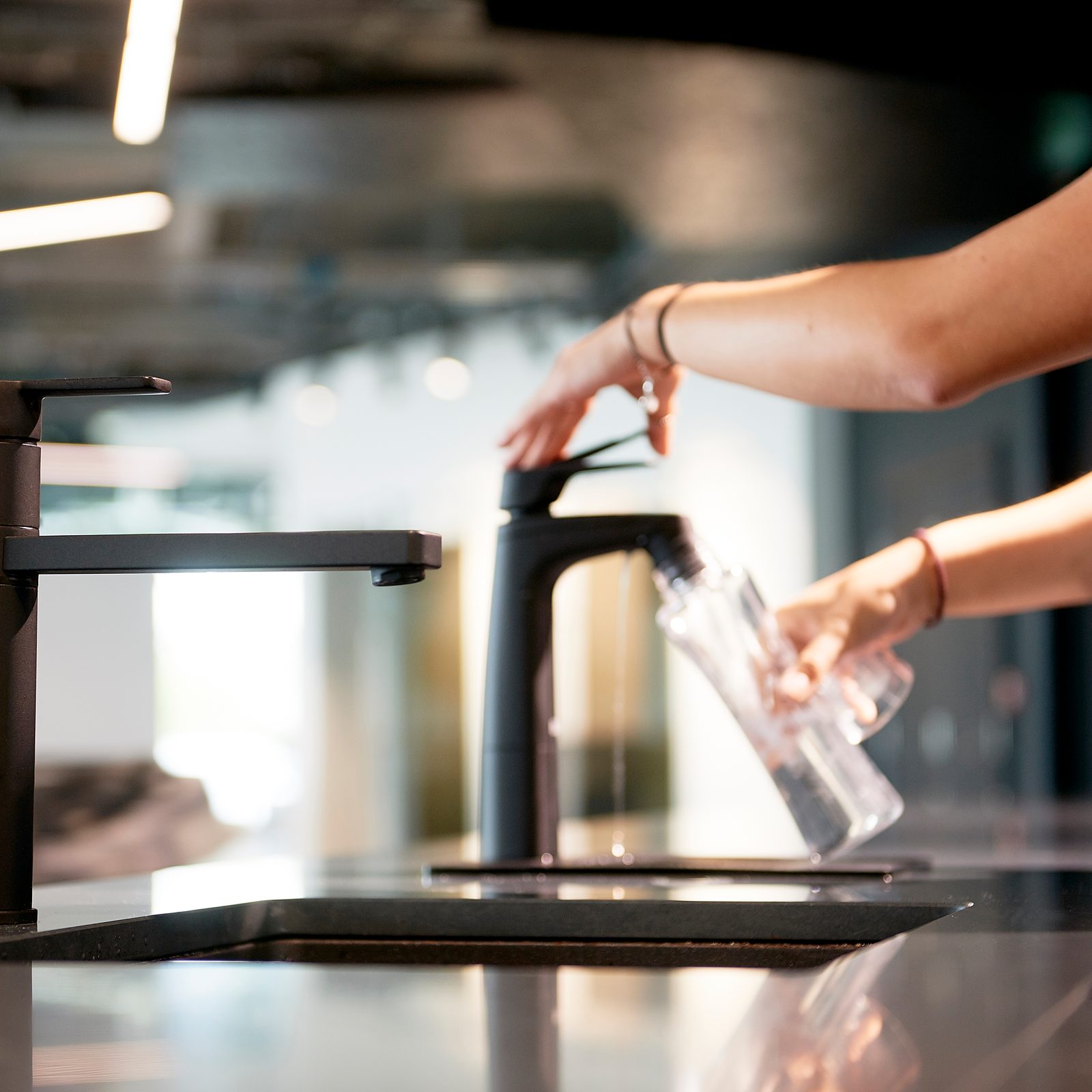 Filling a glass bottle from a matte black Billi XL dispenser beside a paddle mixer
