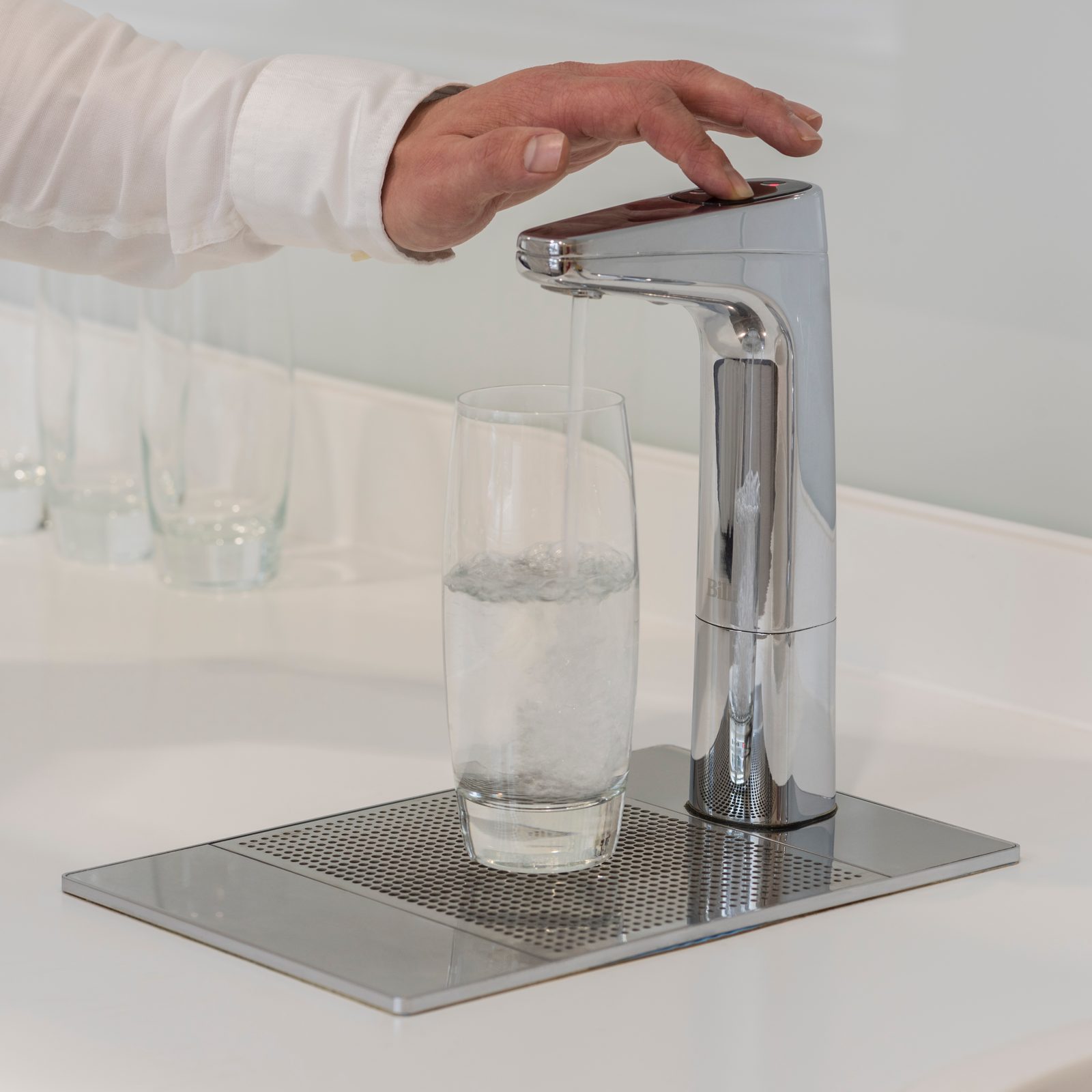 Hand pressing a chrome Billi XT dispenser to fill a glass