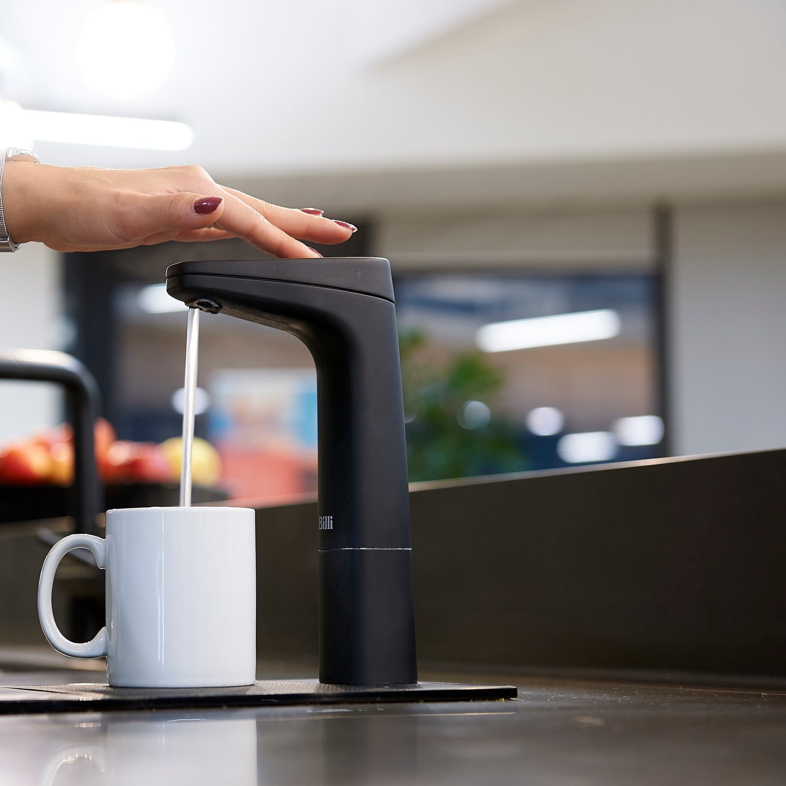 Hand pressing a matte black Billi XT dispenser to fill a mug